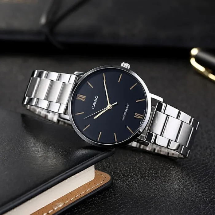 Casio MTP-VT01D-1B — Black dial bracelet watch displayed beside a notebook
